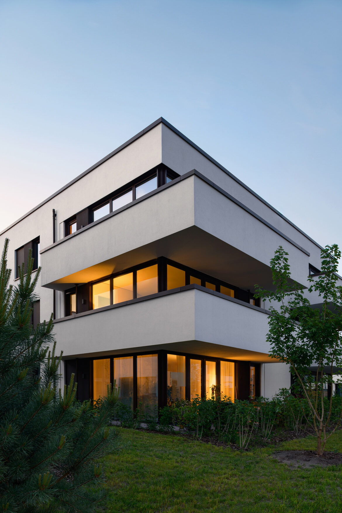 Evening architectural photograph of a residential building with warm light glowing from the windows and balconies